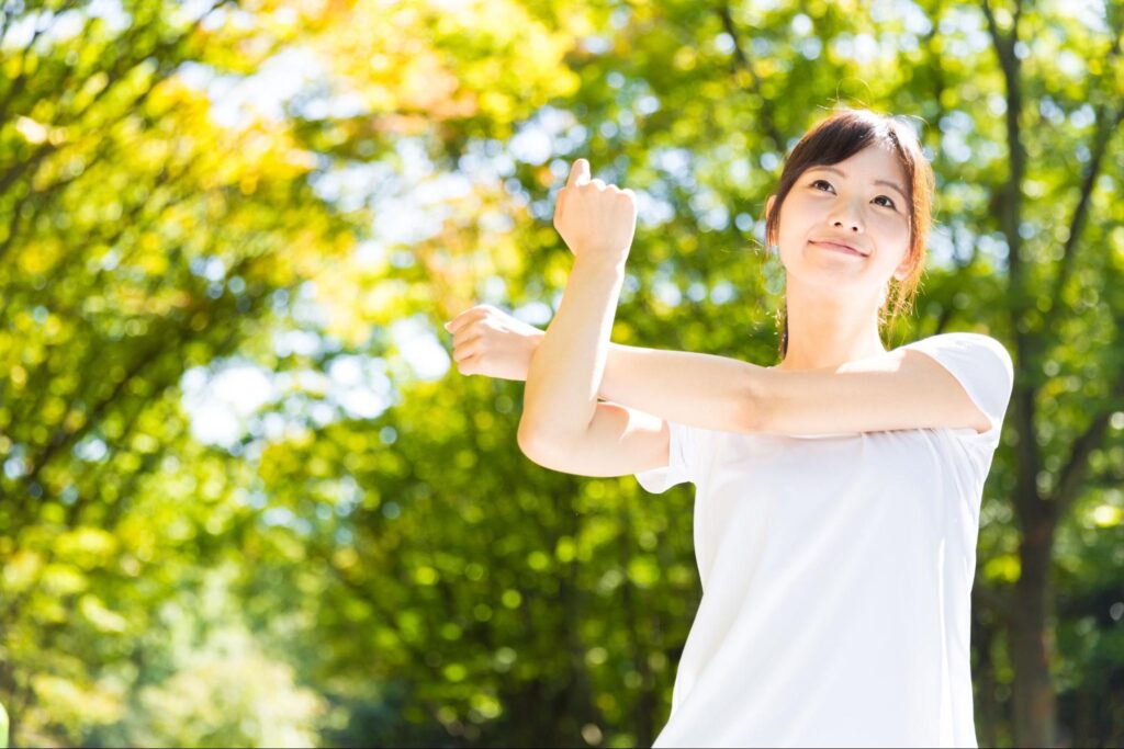緑に囲まれて腕周りのストレッチをする女性の画像