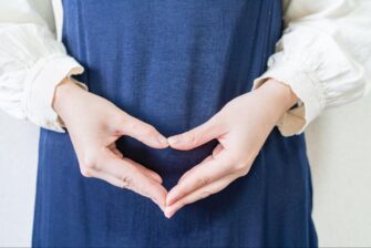 お腹の前で手でハートを作る女性の画像
