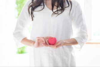 お腹の前でハートマークを持つ女性の画像