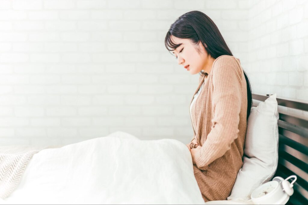 ベッドの中でお腹を押さえる女性の画像